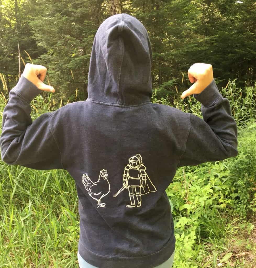 A person photographed from behind, with thumbs pointing at the back of their sweatshirt; the Chicken and the Knight stand together on the back of her hoodie.